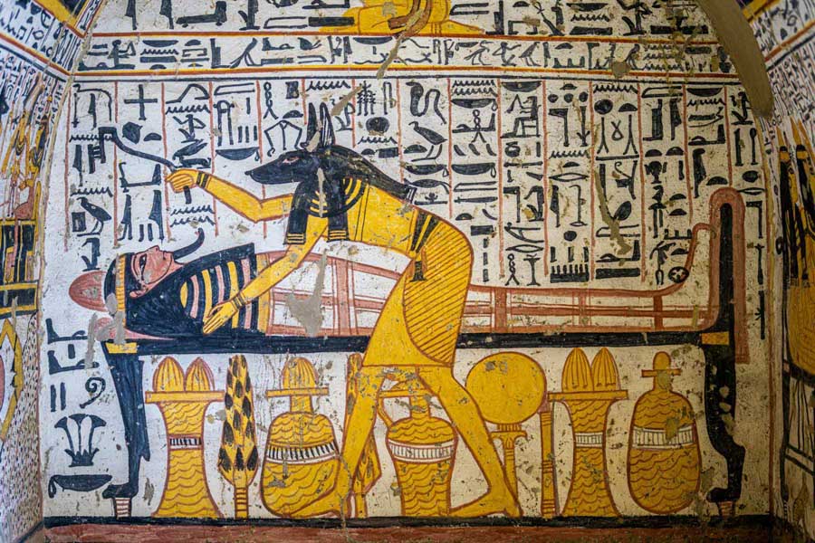 Ancient Egyptian tomb painting of Anubis tending to a mummy.